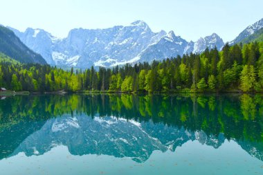 İtalya 'nın Tarvisio kentindeki göl kıyısında bir ormanla birlikte Mangart Dağı' nın üzerindeki lago di fusine inferiore manzarası