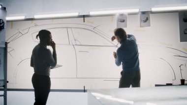 İki farklı otomotiv erkek tasarımcısı gelecekteki elektrikli araba tasarımını tartışıyor ve geliştiriyor. Biri beyaz tahtaya çizimler çiziyor, diğeri tablet bilgisayarı tutuyor. Araba tasarım stüdyosu.