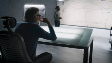 İki farklı otomotiv mühendisi fütüristik elektrikli araba tasarımı taslağı geliştiriyor. Biri beyaz tahtada işaretli, diğeri ışık masasında çalışıyor. Araba tasarım stüdyosu.