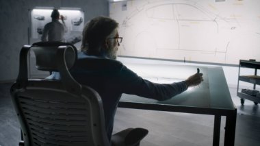 İki farklı otomotiv mühendisi fütüristik elektrikli araba tasarımı taslağı geliştiriyor. Biri beyaz tahtada işaretli, diğeri ışık masasında çalışıyor. Araba tasarım stüdyosu.