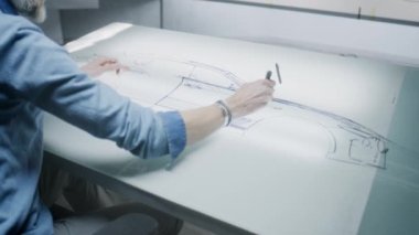 Üst düzey otomotiv erkek tasarımcısı, ışık masasında işaretli araba çizimi yapıyor, gelecekteki elektrikli araba tasarımını geliştiriyor. Modern araba tasarım stüdyosunda çalışıyor..