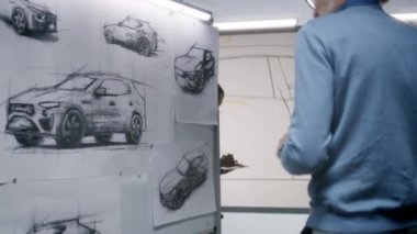 İki farklı otomotiv erkek tasarımcısı gelecekteki elektrikli araba tasarımını tartışıyor ve geliştiriyor. Biri beyaz tahtaya çizimler çiziyor, diğeri tablet bilgisayarı tutuyor. Araba tasarım stüdyosu.