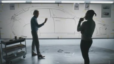 İki farklı otomotiv erkek tasarımcısı çizimi tartışıyor, keçeli kalemle çiziyor, beyaz tahtada gelecekteki elektrikli araba tasarımını geliştiriyor. Modern araba tasarım stüdyosunda çalışıyorlar..