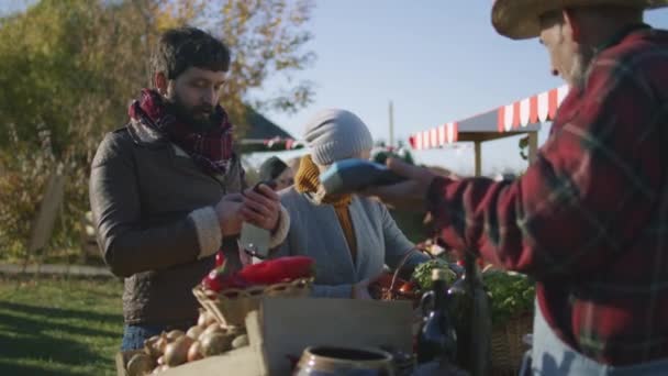 시장에서 쇼핑하는 빈틈없는 사람은 스마트폰을 사용하여 농부에게 물건을 데대한 대가를 — 비디오