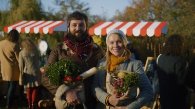 Eşler, meyve ve sebze dolu çantalarla poz verip kameraya bakıyor, çiftçi pazarından alışveriş yaptıktan sonra gülümsüyor ve mutlu oluyorlar. Dikey görünüm