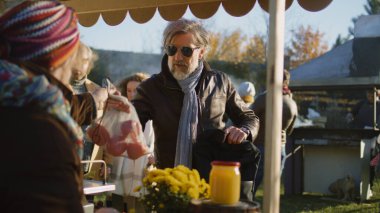 Kıdemli adam sebze alıyor, akıllı telefon kullanarak temas kurmadan satın alımlar için para ödüyor. İnsanlar arka planda yürürken ve alışveriş yaparken. Yerel çiftçi pazarı ya da açık hava pazarı. Vejetaryen ve organik yiyecekler. Tarım.