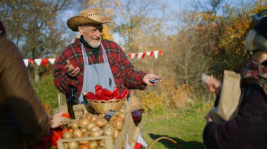 Kıdemli çiftçi yaşlı bir kadına kağıt eko torba içinde mal veriyor. Satın almak için ödeme yapan kadın. Yerel çiftçi pazarı ya da sonbahar fuarı. Vejetaryen ve organik yiyecekler. Tarım. Satış sistemi.