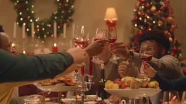Mutlu çok kültürlü aileler Noel 'i ya da yeni yılı kutluyor, şarap kadehlerini kaldırıyor. Farklı yemek ve mumlarla servis edilen tatil masası. Evde aile yemeği için sıcak bir ortam. Şerefe..