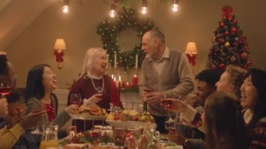 Mutlu çok kültürlü aileler Noel 'i ya da yeni yılı kutluyor, kadehleri şarapla kaldırıyor. Bulaşık ve mumlarla tatil masası servis edildi. Evde aile yemeği için sıcak bir ortam. Şerefe..