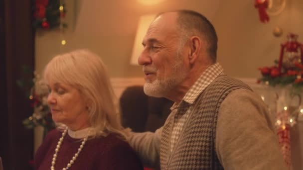 幸せな高齢者のカップル笑って家族と話しています クリスマスや新年を祝う祖父母2023 家庭でのクリスマスディナーの暖かい雰囲気 クリスマスルームの装飾 — ストック動画