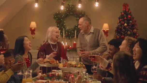 クリスマスや新年を祝う幸せな多文化家族 ワインとグラスを上げます 料理やキャンドル付きの休日のテーブルを提供します 家庭でのクリスマスディナーの暖かい雰囲気 — ストック動画
