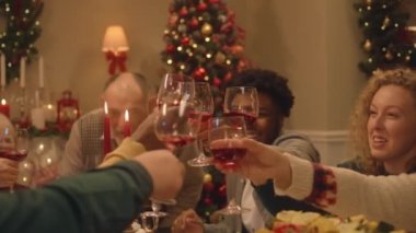 Mutlu çok kültürlü aileler Noel 'i ya da yeni yılı kutluyor, şarap kadehlerini kaldırıyor. Farklı yemek ve mumlarla servis edilen tatil masası. Evde aile yemeği için sıcak bir ortam. Şerefe..