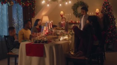 Mutlu çok kültürlü aileler Noel 'i ya da 2023 yılını kutluyor, hediyelerimizi değiş tokuş ediyoruz. Farklı yemek ve mumlarla servis edilen tatil masası. Aile içinde sıcak bir Noel yemeği..