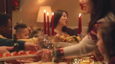 Mutlu çok kültürlü aileler Noel 'i ya da 2023 yılını kutluyor, konuşuyor ve yiyor. Farklı yemek ve mumlarla servis edilen tatil masası. Aile içinde sıcak bir Noel yemeği..