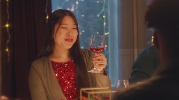 アジアの女性はワイン トーク 笑顔を飲む クリスマスや新年を祝う多文化の友人2023 休日のテーブルを提供 自宅でクリスマスディナーの暖かい雰囲気 クリスマスパーティー — ストック動画