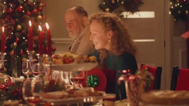 女が現れる クリスマスや新年を祝う幸せな多文化家族2023 異なる料理やキャンドルと休日のテーブルを提供します 家庭でのクリスマスディナーの暖かい雰囲気 — ストック動画