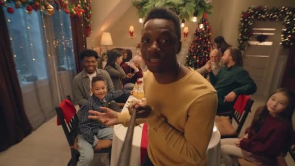 アフリカ系アメリカ人の男性の自撮り棒のレコードビデオ 料理とテーブルを示しています クリスマスや新年を祝う多文化家族 自宅で家族のクリスマスディナーの雰囲気 カメラビュー — ストック動画