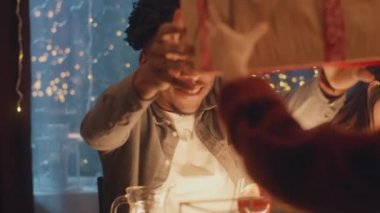 Şaşırmış Afrikalı Amerikalı adam hediyesini açıyor. Noel 'i ya da 2023 yılını kutlayan çok kültürlü arkadaşlar. Farklı yemeklerle servis edilen tatil masası. Noel partisinin atmosferi evde.