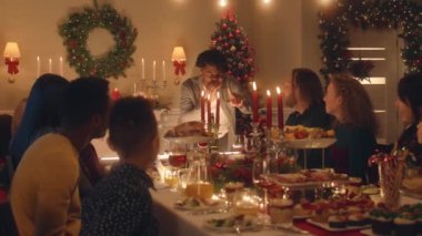 Afrikalı Amerikalı bir adam genç bir çocuğa hediye veriyor. Mutlu aile alkışları ve Noel 'i ya da 2023 yılını kutlamak. Tabaklar ve mumlarla dolu bir tatil masası. Aile yemeği için sıcak bir ortam..