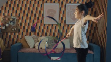 Genç Asyalı liseli kız jimnastik kurdelesiyle dans ediyor, dikey bacak ayrımını ve kendi etrafında dönüşünü gösteriyor. Ritmik jimnastik. Spor hobisi. Karantinadaki fiziksel sağlığı yükseltiyorum. Yavaş çekim.