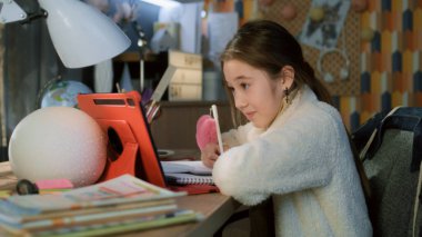 Genç Asyalı kız evde masada oturuyor ve öğretmeniyle konuşuyor. Öğrenci çevrimiçi ders dinler, yeni materyaller yazar ve tablete çalışmalar yapar. Modern tasarım. Uzaktan öğrenme konsepti. Uzak