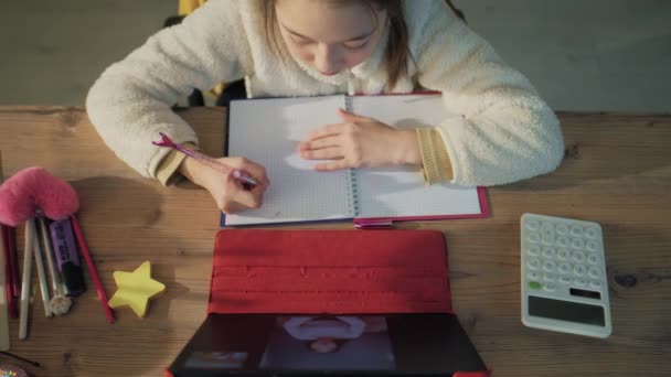 年轻的亚洲女孩坐在舒适的家中餐桌旁 与成年教师交谈 女学生在网上听课 写下新材料 并在平板电脑上学习 远程会议 向上看 — 图库视频影像