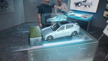 İki Mühendis Geliştirici, geleceğin holografik masasının yanındaki tasarım stüdyosunda duruyorlar ve 3 boyutlu bir araba kazası test simülatöründe test yapıyorlar.