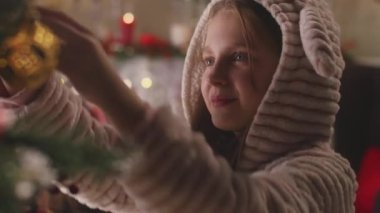 Pijamalı genç kız balo seçiyor ve annemle Noel ağacı süslüyor. Noel 'den ya da yeni yıldan önce aile oturma odası hazırlığı. Kış tatillerinin sıcak atmosferi. Yakın çekim görüntüsü. Yavaş çekim.