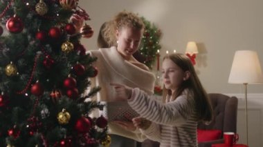 Annesiyle mutlu genç bir kız Noel ağacını toplar ve oyuncaklarla süslüyor. Babam duvara Noel çelengi asıyor. Aile, kış tatili ya da yeni yıl için ev hazırlıyor. Yavaş çekim.