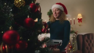 Anne ile kızı topları ve oyuncakları seçiyor, Noel ağacını süslüyor. Pijamalı genç kız, Noel tatilinden önce evi hazırlamak için anneye yardım ediyor. Sıcak bir evde kışın büyüsü. Yavaş çekim.