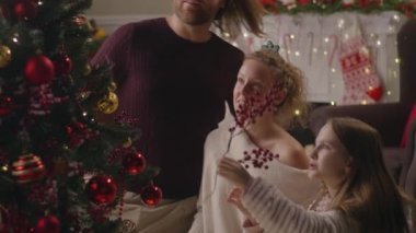 Aile birlikte oturma odasında oturuyor ve Noel ağacını dallarla süslüyor. Duvarda yanıp sönen çelenk ışıkları. Kışın sıcacık bir evde tatil. Yavaş çekim