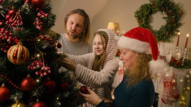 Ailesi oyuncak seçen ve Noel ağacı süsleyen genç bir kız. Aile, kış tatilinden önce ya da yeni yıldan önce oturma odasını hazırlıyor. Konforlu evde Noel atmosferi. Yavaş çekim.