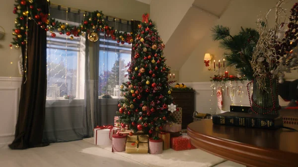 Tree with balls, toys, flashing lights, wrapped gifts and present boxes stands in living room. Christmas and New Year festive interior decoration. Atmosphere in cozy apartment on winter holidays.