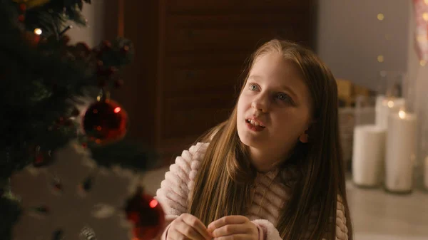 부드러운 파자마를 소녀는 바닥에 장난감으로 크리스마스 트리를 장식하고 웃으며 집에서 — 스톡 사진