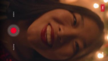 Asyalı kadının dikey görüntüsü kamerada ya da telefonda zamanlayıcı ayarlıyor. Mutlu çok kültürlü aile grup fotoğrafı çeker. Noel 'i ya da yeni yılı kutluyorlar. Tabaklar ve mumlarla dolu bir masa. Kamera görünümü.