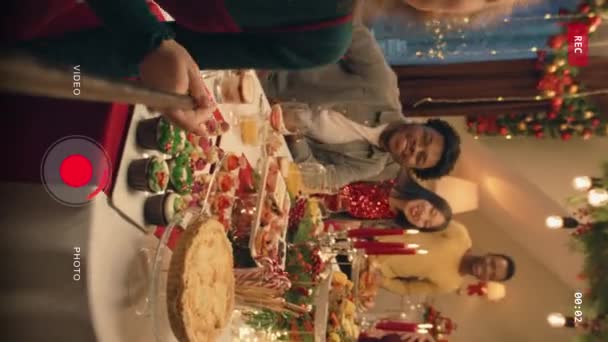 自撮り棒を持つ白人女性の垂直撮影は家族のグループ写真をとります クリスマスや新年を祝う多文化家族 自宅で家族のクリスマスディナーの雰囲気 カメラビュー — ストック動画