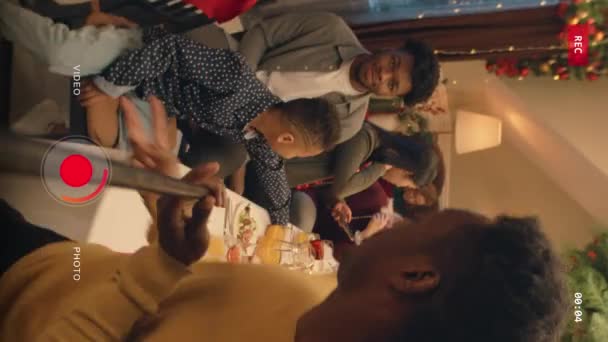 アフリカ系アメリカ人の男性の垂直ショットは ビデオを記録し 料理とテーブルを示します クリスマスや新年を祝う多文化家族 自宅で家族のクリスマスディナーの雰囲気 カメラビュー — ストック動画