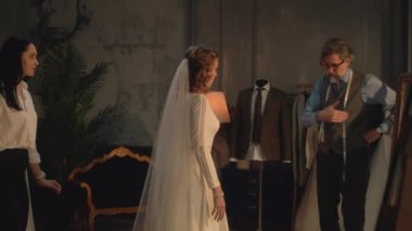 Cinematic shot of happy woman in wedding dress and veil walking in front of the mirror. Bride on fitting wedding dress in designer atelier or wedding salon. Concept of fashion and couturier.