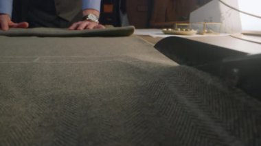 Close-up shot of tailor cutting textile according to sketch using scissors for sewing. Process of making clothes in luxury designer atelier or tailoring studio. Fashion and hand craft concept.