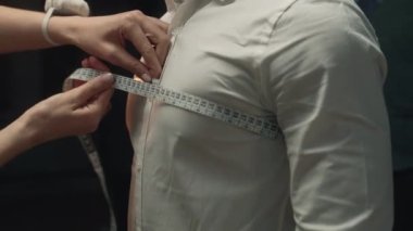 Cinematic shot of female tailor takes measurements of client for wedding or business suit shirt. Work in luxury designer atelier or tailoring studio. Concept of fashion, handmade and couturier.
