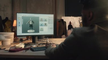 African American tailor or fashion designer creates clothes and develops future wear collection in 3D modeling program. He works in luxury workshop or tailoring studio on laptop. Fashion concept.