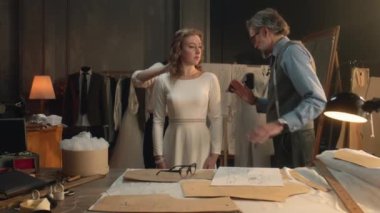 Cinematic shot of tailors taking measurements of woman for wedding dress. Bride on fitting wedding dress in luxury designer atelier or tailoring studio. Concept of fashion, handmade and couturier.