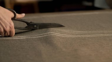 Close-up shot of female tailor cutting textile according to sketch using scissors for sewing. Process of making clothes in luxury designer atelier or tailoring studio. Fashion and hand craft concept.