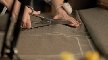 Close-up shot of female tailor cutting textile according to sketch using scissors for sewing. Process of making clothes in luxury designer atelier or tailoring studio. Fashion and hand craft concept.