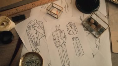 Cinematic shot of table with drawings, needles, threads, buttons, ribbons, soap and ruler. Sketches of clothes, suits and jackets. Designer atelier or tailoring studio. Fashion and hand craft concept.