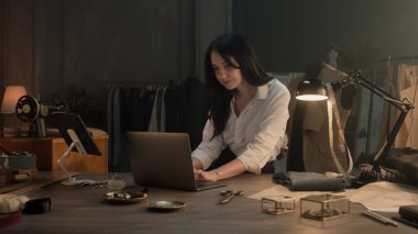 Female tailor works on new clothes collection in luxury atelier. She draws modern design of tailored suits on computer and tablet, chooses color and type of textile. Concept of fashion. Slow motion