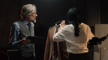 Male and female tailors work on business or wedding suit. Man draws sketch on tablet computer. Mannequin in tailored suit in designer atelier or tailoring studio. Fashion and hand craft concept.