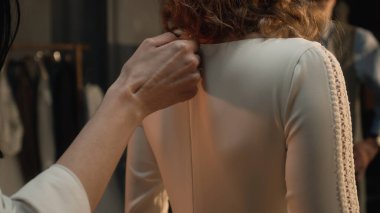 Close-up shot of tailor zipping up wedding dress on woman in front of mirror. Bride on fitting wedding dress in luxury designer atelier or wedding salon. Concept of fashion, handmade and couturier.