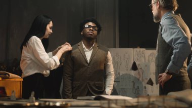 Female tailor measures sleeve of tailored suit, discusses with client size and fabric. African American businessman wears wedding business jacket and talks with male designer. Fashion concept.