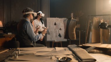 Tailors wearing VR headset with wireless controllers. They working in luxury atelier or tailoring workshop and creating weeding suit in virtual reality. Concept of technologies of future in business.